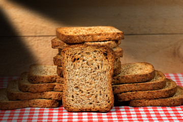 Healthy rusks of wholemeal flour on a table with checkered tablecloth and wooden wall