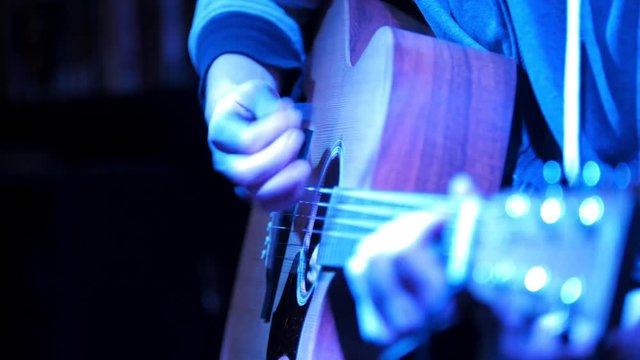 Close up view of guitarist plays acoustic guitar in night club