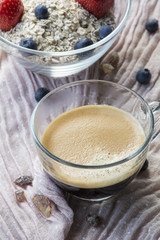 One cup of black coffee and glass bowl with flakes, berries and one spoon on the pink tissue