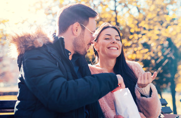 Loving couple sitting on the bench in the park and eating popcor