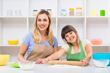 Happy mother and her daughter enjoy rolling dough together and making cookie.