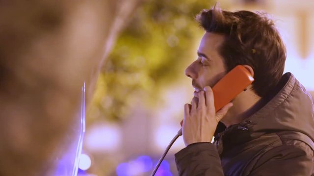 Giovane ragazzo sta parlando a un telefono pubblico di notte