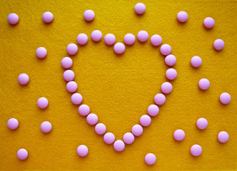 heart made of pink pills on yellow felt background and pills scattered around