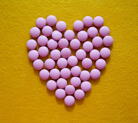 heart made of pink pills on bright yellow felt background