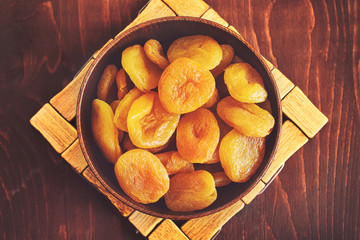 Dried apricots in bowl on wooden background. Top view