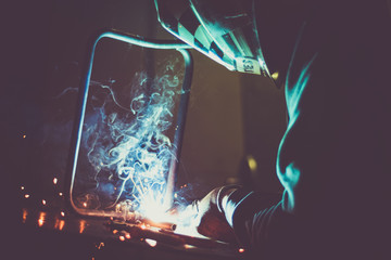 Industrial worker welding a loop made of round pipe on work table, producing smoke, sparks and...