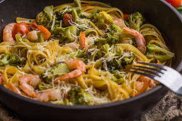 Pasta linguine with shrimps and broccoli in dripping pan on wooden background.