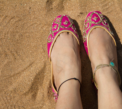 A lady wearing a pair of pink traditional Indian women's shoes (jutis) at the Anjuna beach in north Goa, India