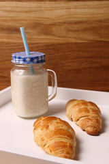 Croissant and milk in a jar on a white tray.