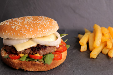 Homemade cheeseburger with arugula, mini tomatoes and homemade French fries on the stone slate board.