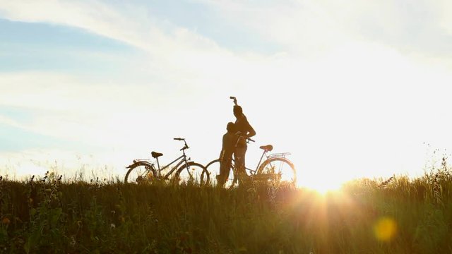 Happy father and son takes selfie near bikes in sunset lights. Family makes self portraits photos with cell phone in beautiful sunny landscape. Silhouettes of anonymous man, child over sky background