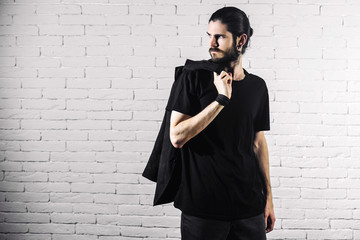 young bearded gothic hipster man standing on a brick wall background. a man dressed in black