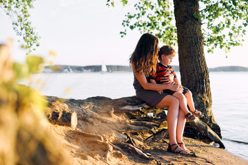 Young mother resting with his young son in the summer at sunset on the lake under the tree
