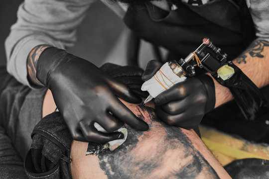 Tattoo master in black gloves, tattoo on the skin of black ink tattoo of his client in the salon.