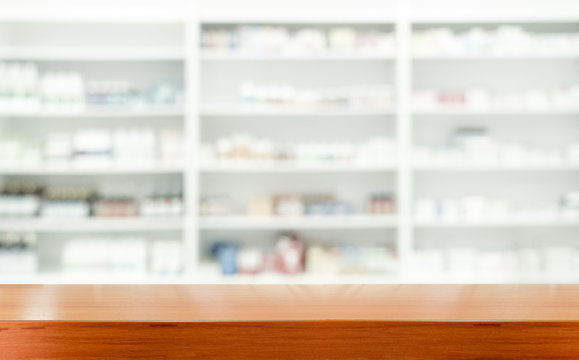 Brown wooden tabletop with blurred pharmacy or medicine shelf at the hospital