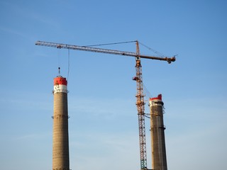 A view of power plant chimneys being demolished by a crane