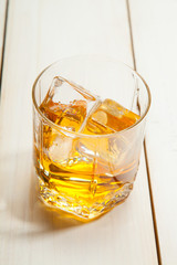 glass of whiskey with ice on a white wooden background