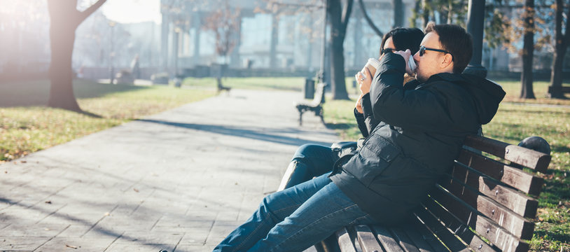 Couple sitting on park bench and drinking coffee