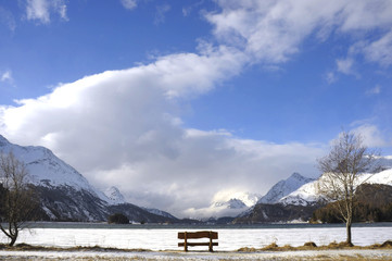 bench looking solitary at frozen Sils lake in Engadin Switzerland with snow Alps mountains