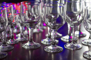 Lots of clean empty glasses of drinks on the bar in a nightclub. Glare and reflections on the glasses in the dark