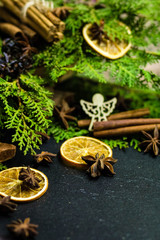 Christmas tree branch with spices of cinnamon, orange and anise. wooden star on a dark background