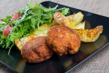 Close up of a black plate with fish meatballs with parsley and f