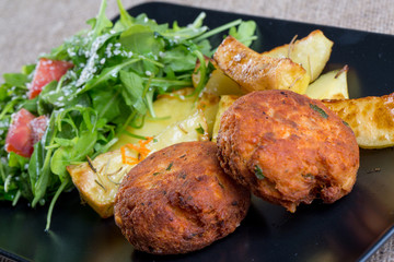 Close up of a black plate with fish meatballs with parsley and f