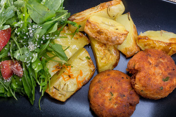 Close up of a black plate with fish meatballs with parsley and f