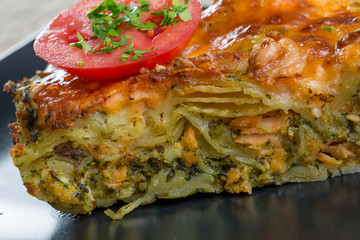 Close up of Salmon lasagna with tomato slice on a black plate