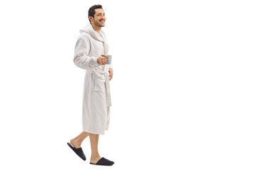 Young man in a bathrobe holding a cup and walking - obrazy, fototapety, plakaty