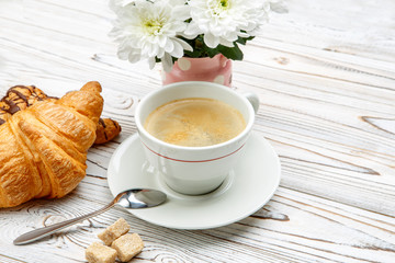two fresh croissants and coffee, flowers on wooden background