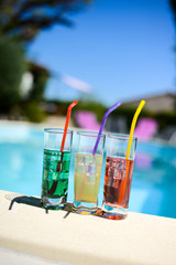 three tropical colorful drink cocktail with a straw on the poolside of resort swimming pool with nobody