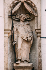 Riga Latvia. Close Ancient Statue Of Man With Cross And Book In Hands On The Facade Of St. Peter Church,