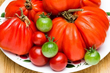Red and green tomatoes on a saucer red and green. Against the background of wood.