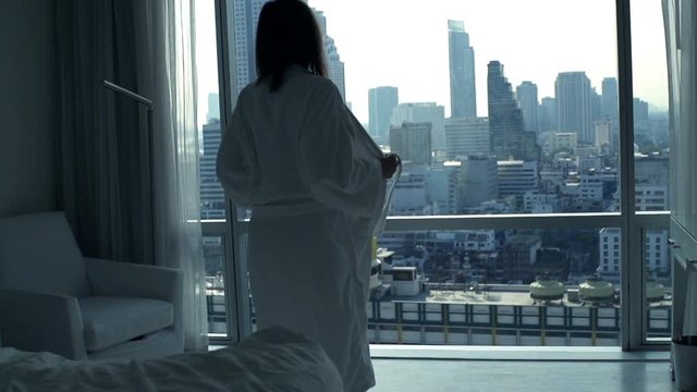 Silhouette of woman taking off bathrobe and stretching arms by window at home, super slow motion 240fps
