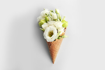 Waffle cone with bouquet of beautiful flowers on white background