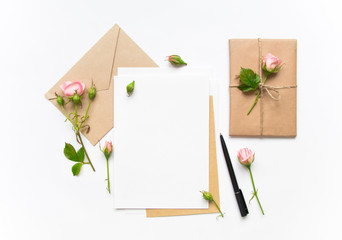 Letter, envelope and gift on white background. Invitation cards, or love letter with pink roses. Holiday concept, top view, flat lay