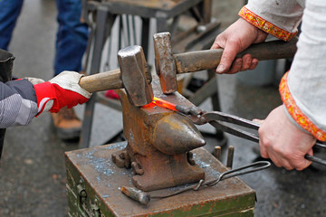 The hands of a blacksmith and learner forging hot iron on the anvil.