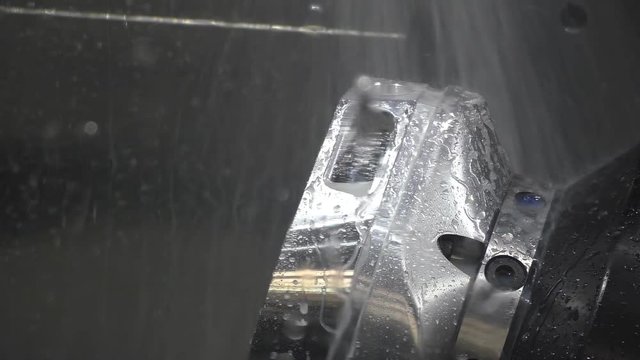 Close up of CNC milling machine cutter doing finishing touches on big shiny workpiece using plenty of coolant