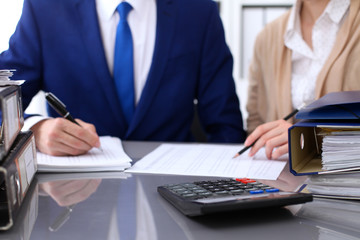 Binders with papers are waiting to be processed with businessman and secretary back in blur. Internal Revenue Service inspector checking financial document.