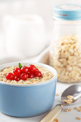 Oat flakes in a blue bowl decorated with fresh currant. Milk and oat jar in background.