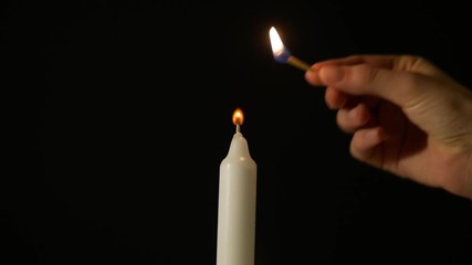A woman lights a candle on a black background, and then blows it.