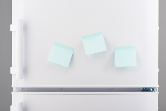 Three blank light blue sticky paper notes on white refrigerator