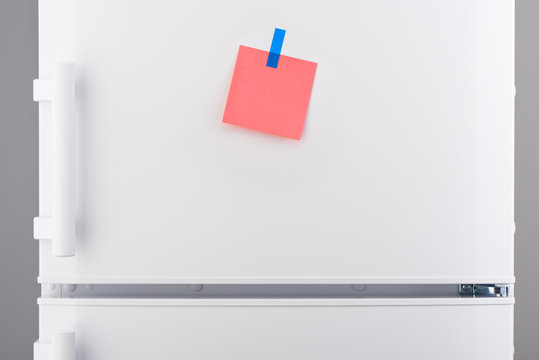 Pink paper note attached with blue sticker on white refrigerator