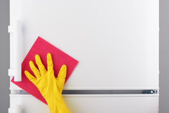 Hand in yellow glove cleaning white refrigerator with pink rag