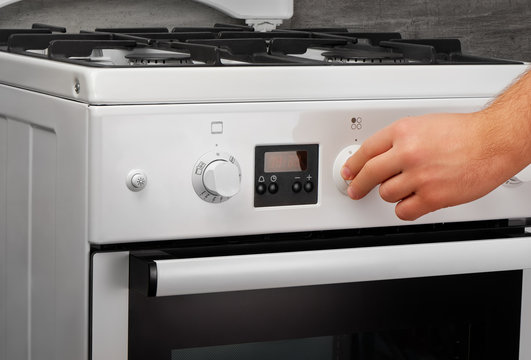 Male hand turning on white kitchen gas stove on gray