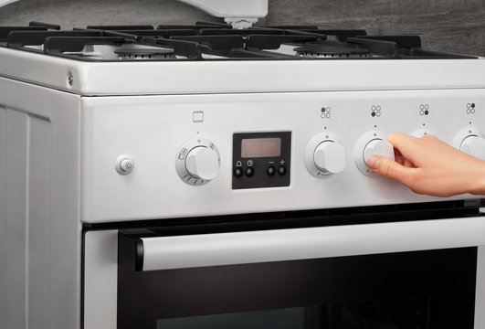 Female hand turning on white kitchen gas stove on gray