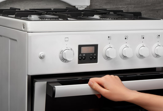 Female hand opening oven in white kitchen gas stove