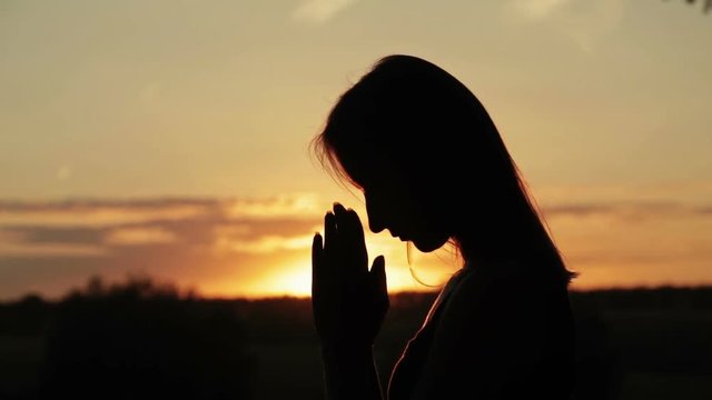 Silhouette of young woman praying in the forest at sunset. Sunset light, sun lens flares, golden hour. Religion, spiritual and nature concept