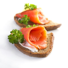 Two sandwiches with smoked salmon, sauce and parsley on a white background